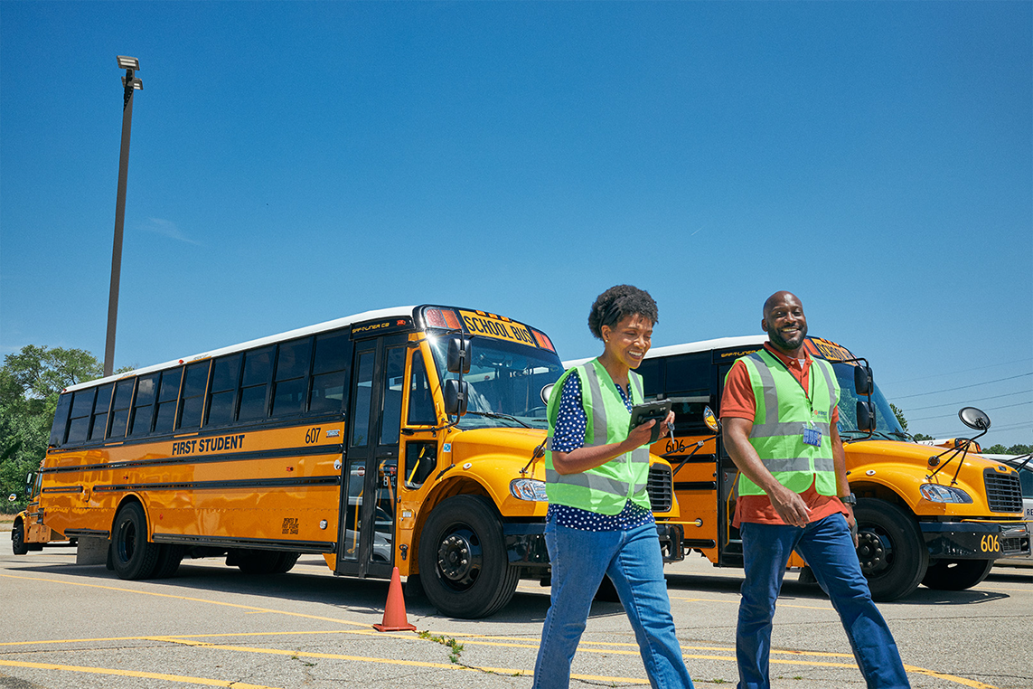 Two staff members walking away from parked school busses.